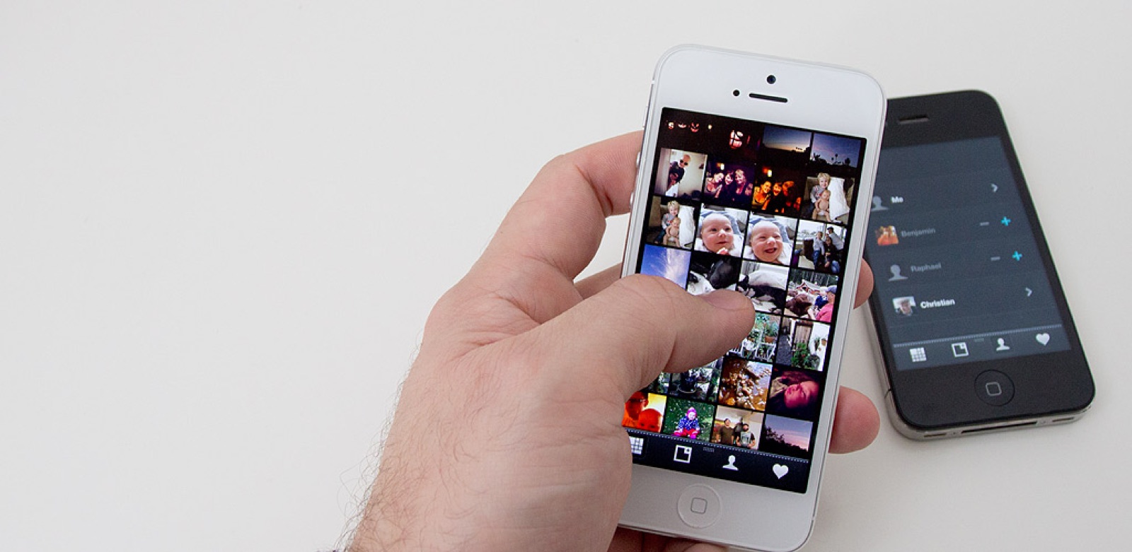 A hand holding a white iPhone 5 showing Pear's photo grid (a tight mosaic of personal photos), with a black iPhone laid next to it showing the contact-share view (Me, Benjamin, Raphael, Christian).